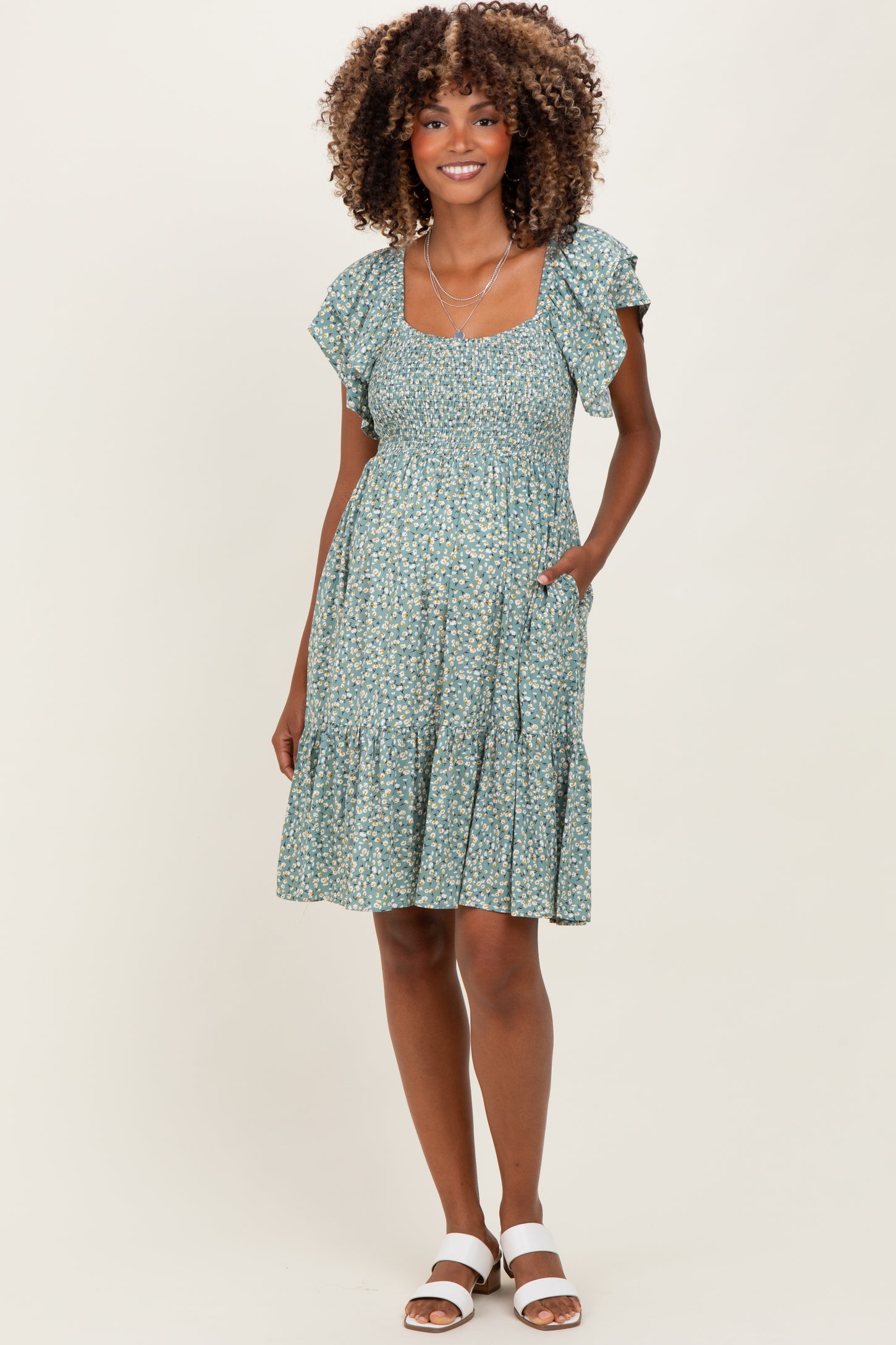 woman wearing a green floral maternity dress with ruffled sleeves and a tiered skirt
