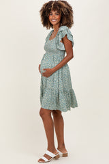 woman wearing a green floral maternity dress with ruffled sleeves and a visible baby bump