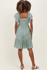woman wearing a green floral maternity dress with ruffle sleeves and a tiered skirt, showcasing her baby bump from the back