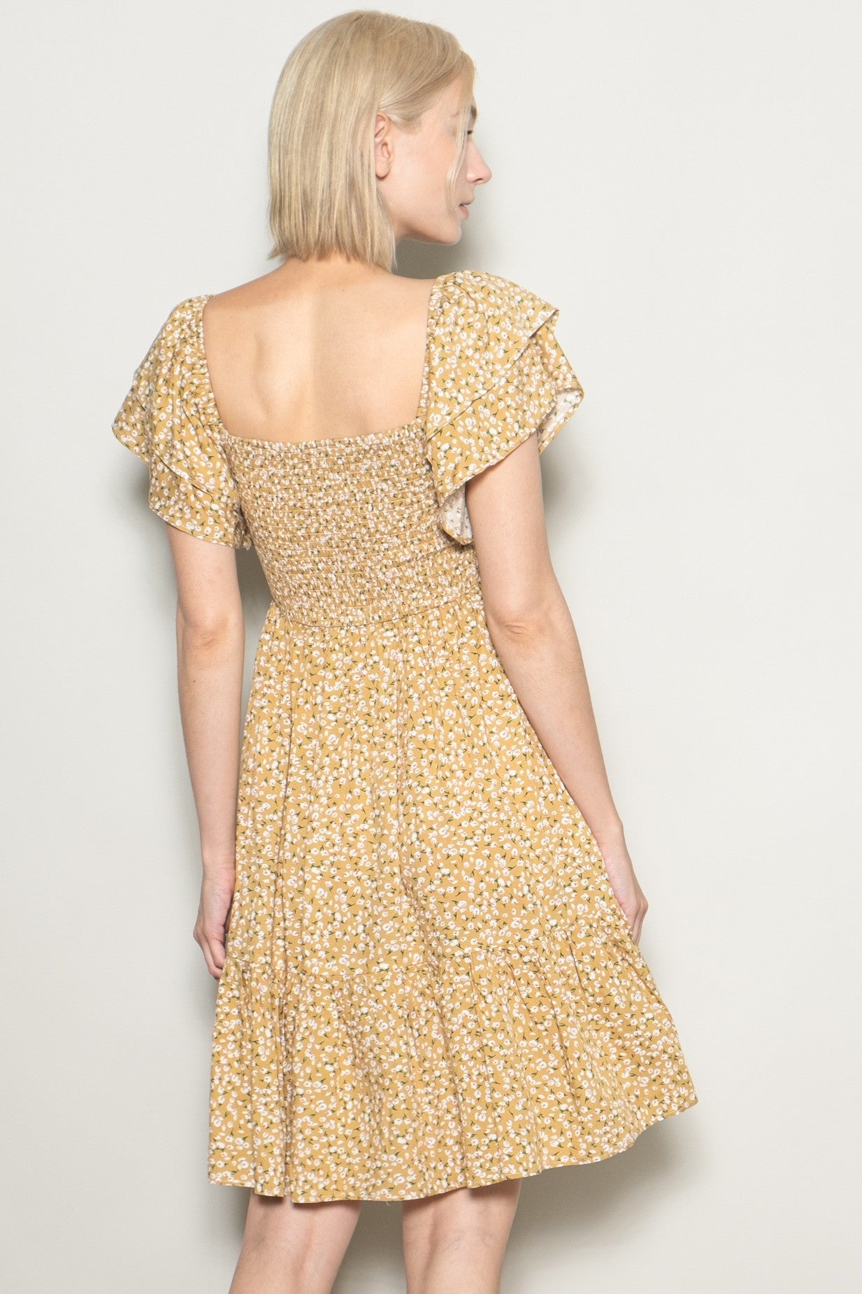 woman wearing a yellow floral short sleeve dress with a smocked bodice and tiered skirt, seen from the back