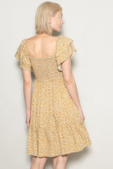 woman wearing a yellow floral short sleeve dress with a smocked bodice and tiered skirt, seen from the back