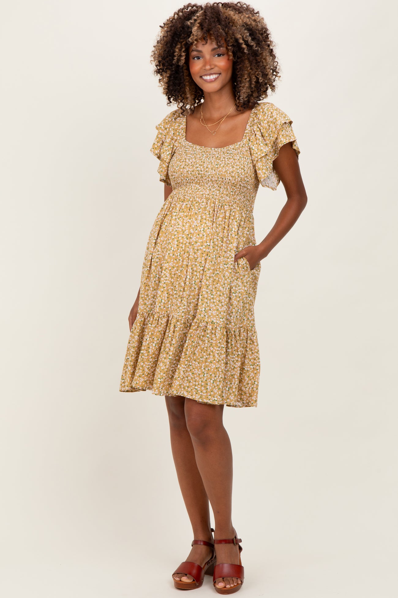 woman wearing a yellow floral maternity dress with short ruffle sleeves and a tiered skirt, showing her baby bump