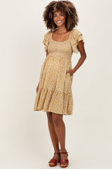 woman wearing a yellow floral maternity dress with short ruffle sleeves and a tiered skirt, showing her baby bump