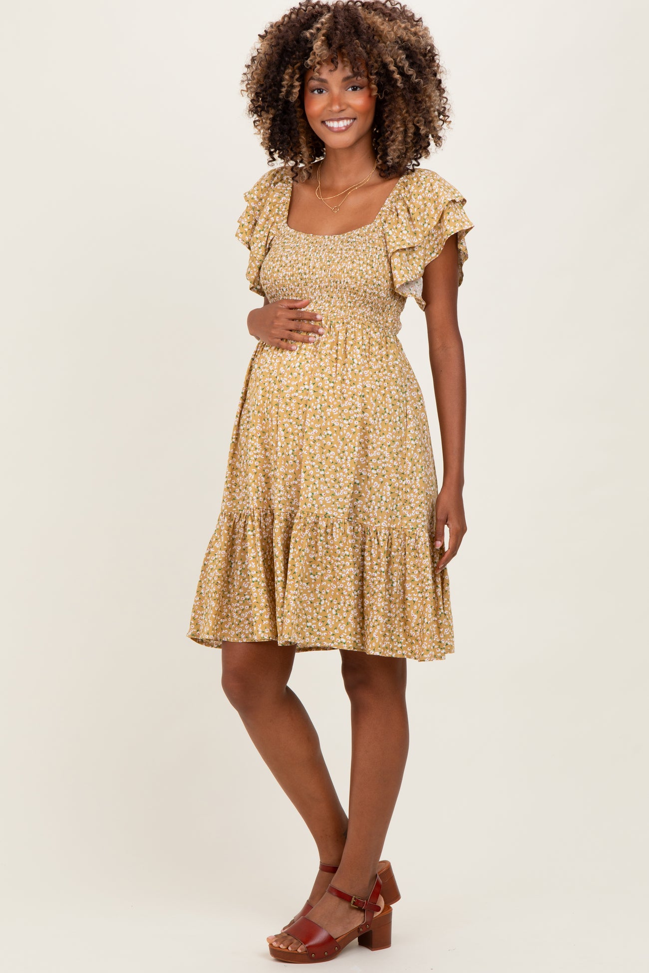 woman wearing a yellow floral maternity dress with ruffled sleeves and a tiered skirt, holding her baby bump