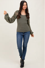 woman wearing a green ribbed long sleeve top with lace-trimmed balloon sleeves and blue jeans