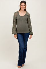 woman wearing a green ribbed maternity top with floral crochet sleeves and blue flared jeans, showing her baby bump