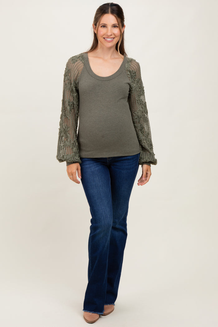 woman wearing a green ribbed maternity top with floral crochet sleeves and blue flared jeans, showing her baby bump
