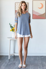 woman wearing a blue striped top with leopard print sleeves and white shorts, standing next to a table with flowers