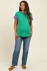 woman wearing a green ribbed maternity top with colorful striped sleeves and a baby bump, paired with blue jeans