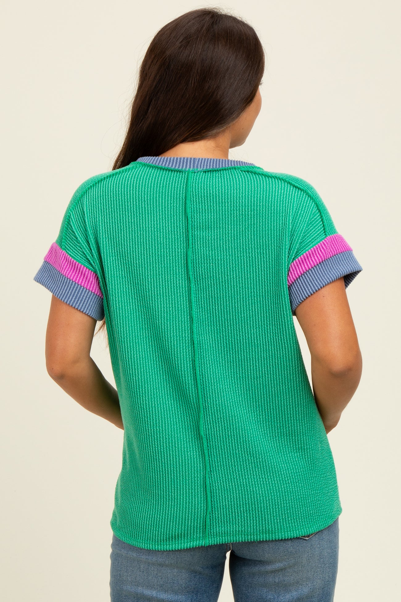 woman wearing a green maternity top with pink and blue accents, showing the back view of the garment