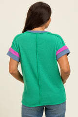 woman wearing a green maternity top with pink and blue accents, showing the back view of the garment