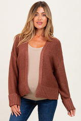 woman wearing a rust-colored open-front maternity cardigan over a beige tank top and showing her baby bump
