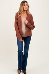 woman wearing a rust-colored maternity cardigan, fitted beige top, and flared jeans, showcasing her baby bump
