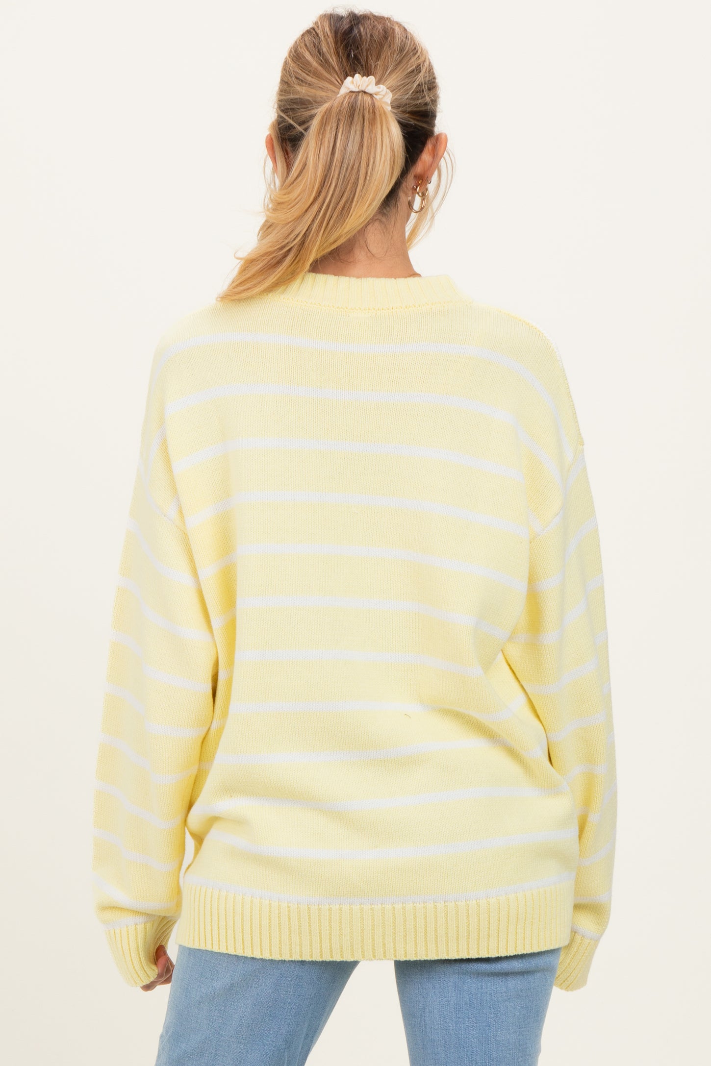 woman wearing a loose-fitting yellow and white striped maternity sweater seen from the back
