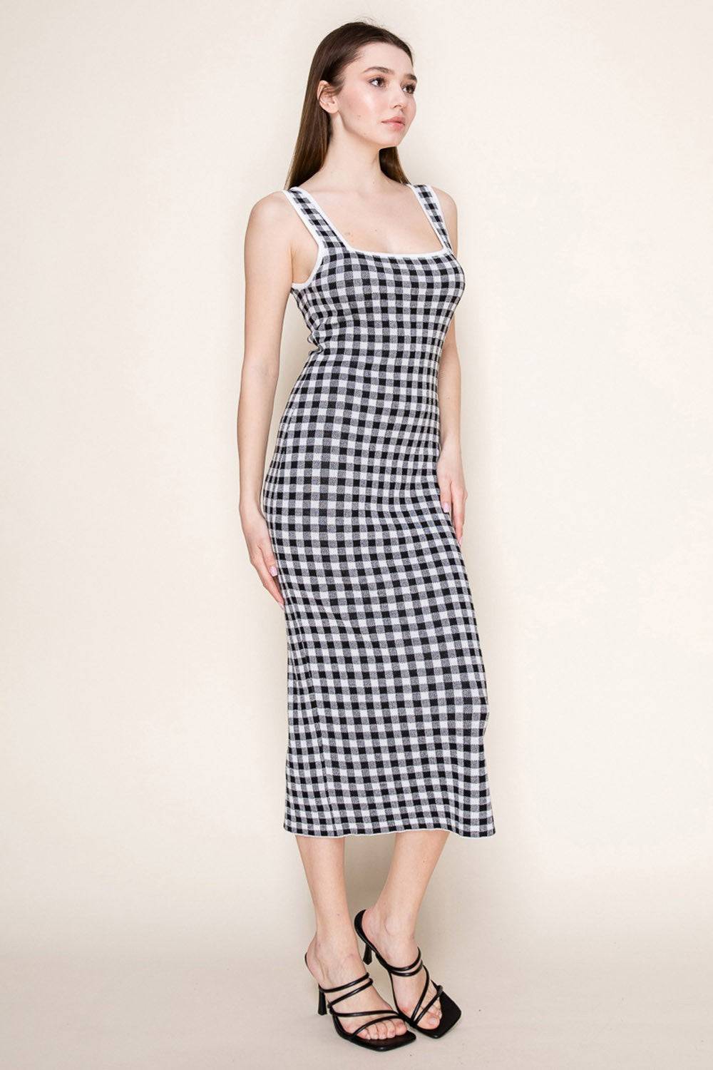 woman wearing a black and white gingham midi dress with a square neckline and slim straps, standing sideways