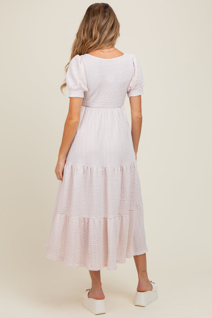 woman wearing a light pink maternity tiered maxi dress with puff sleeves and a scoop back, showing a baby bump