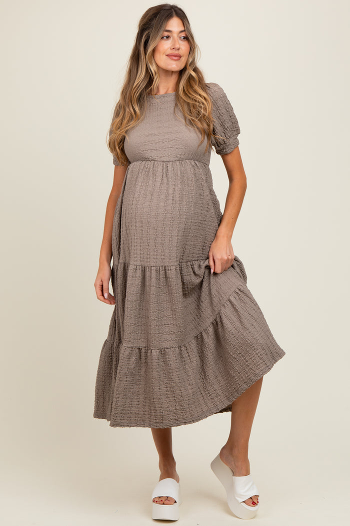 woman wearing a taupe tiered maternity dress with short puff sleeves and a visible baby bump