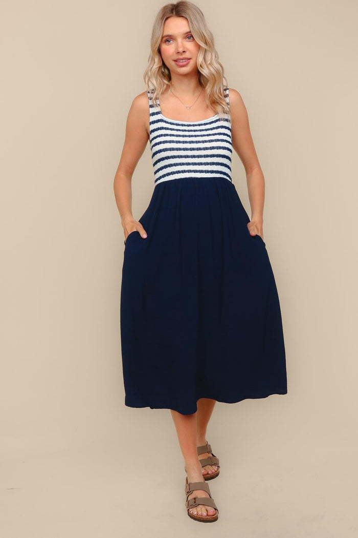 woman wearing a navy blue sleeveless maxi dress with a striped bodice and side pockets