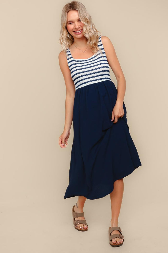 woman wearing a navy blue and white striped sleeveless maxi dress with a flowy skirt and brown sandals