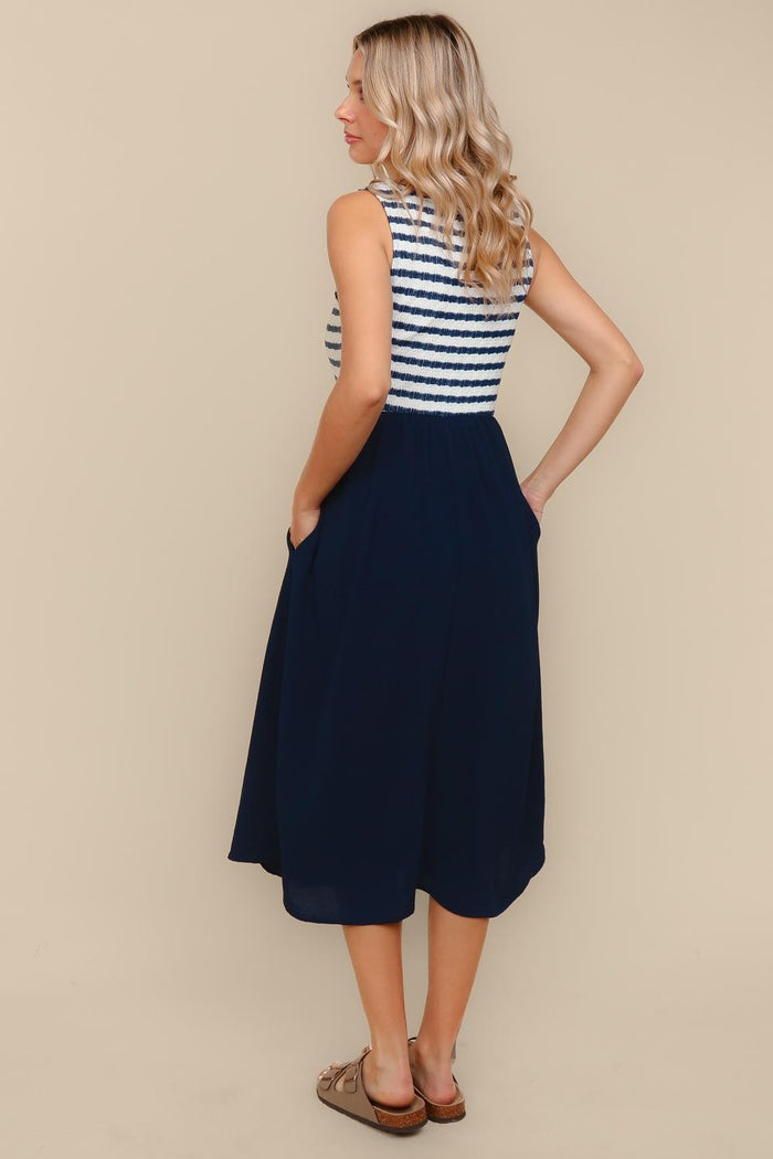 woman wearing a striped sleeveless dress with a navy skirt and pockets, viewed from the back