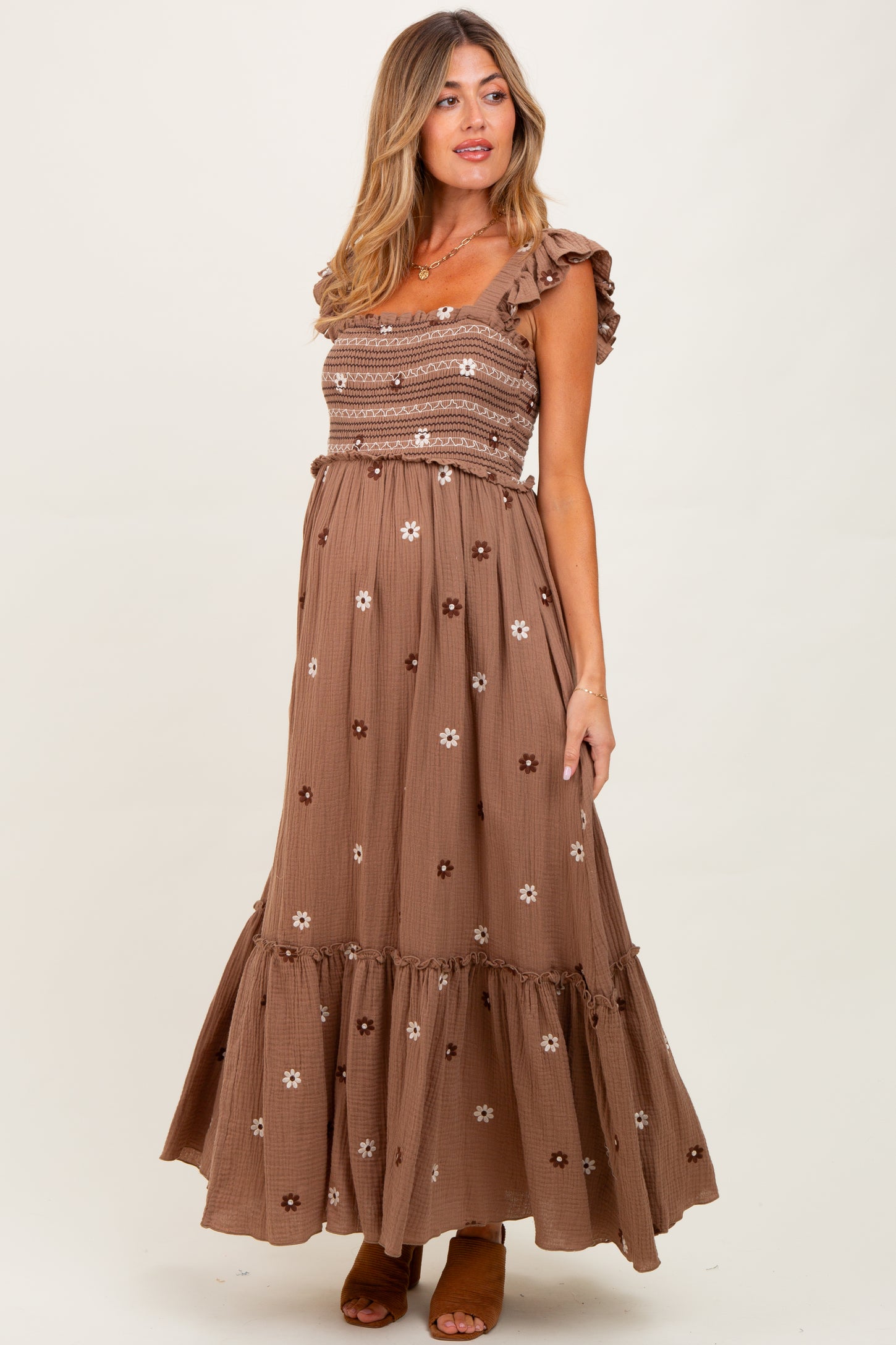woman wearing a brown floral print maternity maxi dress with ruffled straps and a smocked bodice, showcasing her baby bump
