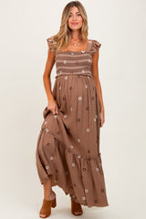 woman wearing a brown floral maternity maxi dress with ruffled sleeves and a smocked bodice, showcasing her baby bump