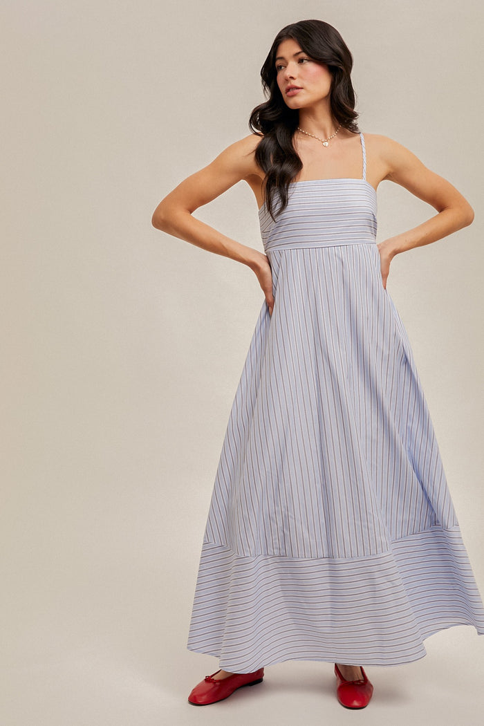 woman wearing a light blue striped maxi dress with spaghetti straps and a flared bottom, paired with red flats