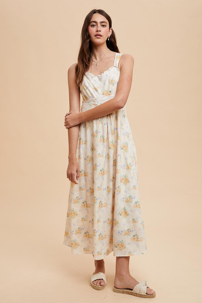 woman wearing a floral maxi dress in soft yellow and white with thin straps and a flowy silhouette