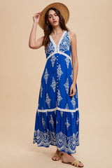 woman wearing a blue patterned maxi dress with a v-neckline and buttons, styled with a wide-brim hat and sandals