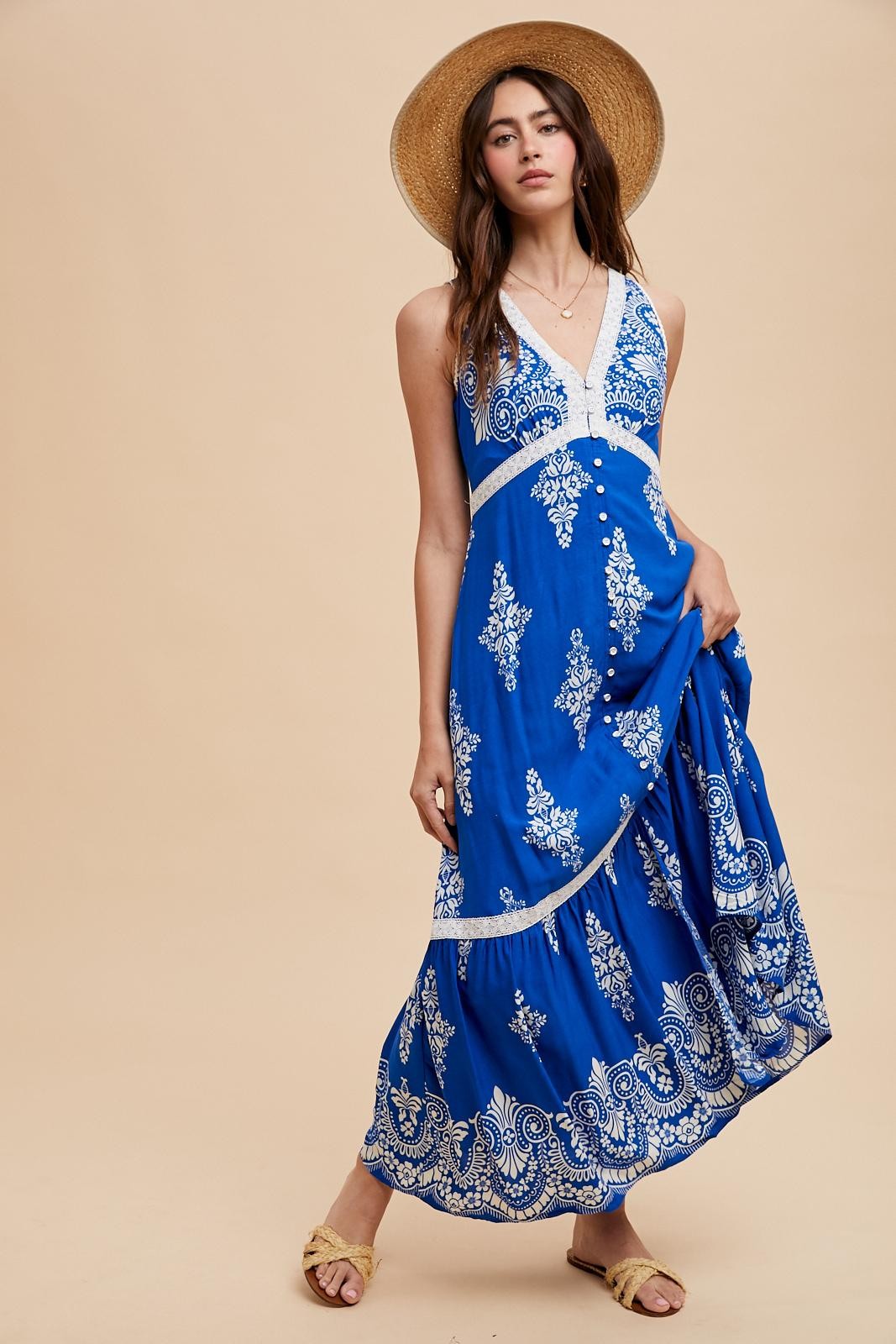 woman wearing a vibrant blue maxi dress with white floral embroidery and a deep V-neck, accessorized with a straw hat