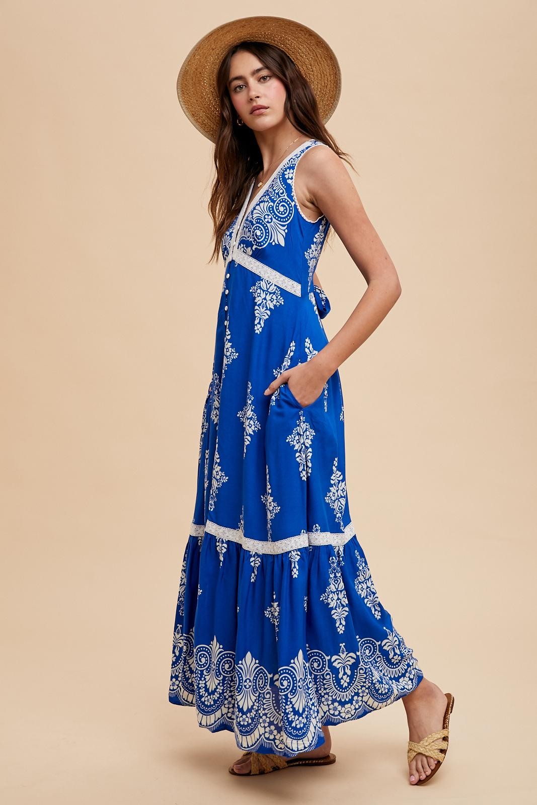 woman wearing a blue maxi dress with white embroidery and pockets, styled with a wide-brimmed hat and sandals
