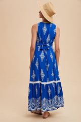 woman wearing a blue maxi dress with white patterns and a tied waist, paired with a wide-brim straw hat