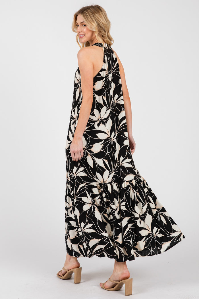 woman wearing a floral black and white maxi dress with a tiered skirt and open back, posing from the side