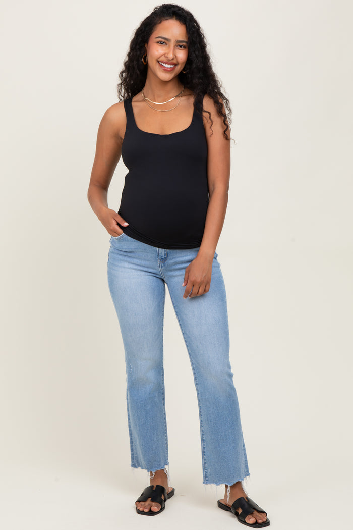 woman wearing a black scoop neck maternity tank top and light blue flared jeans, showing her baby bump