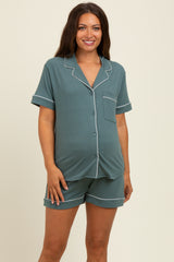 woman wearing a teal maternity sleep set with short sleeves, shorts, and white piping, showing her baby bump