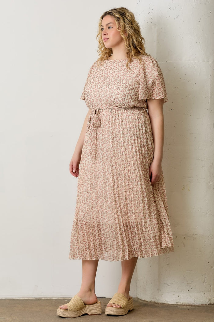 woman wearing a light pink plus size midi dress with a floral pattern and short sleeves, standing against a wall
