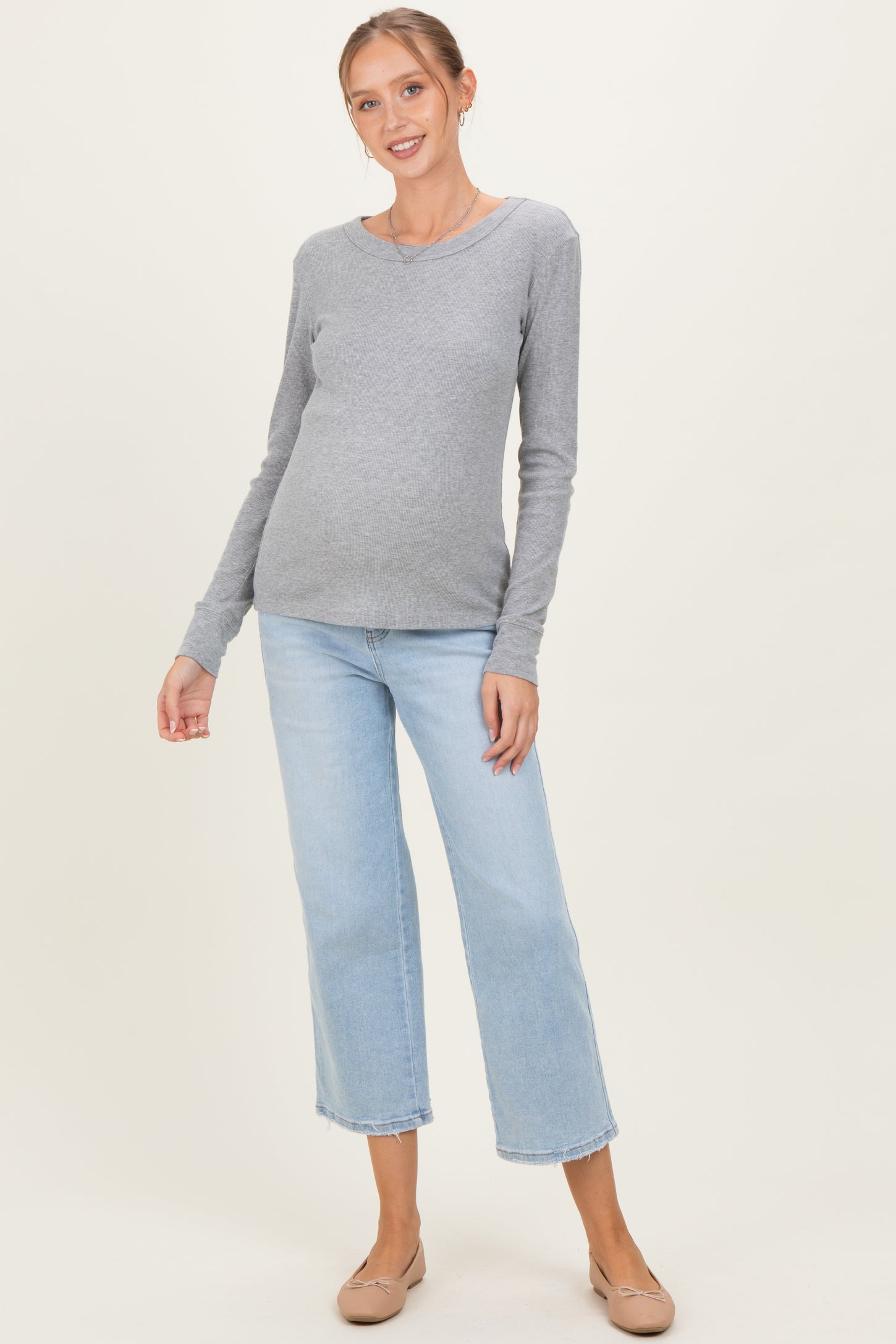 woman wearing a gray long sleeve maternity top and light blue wide leg jeans, showing her baby bump.
