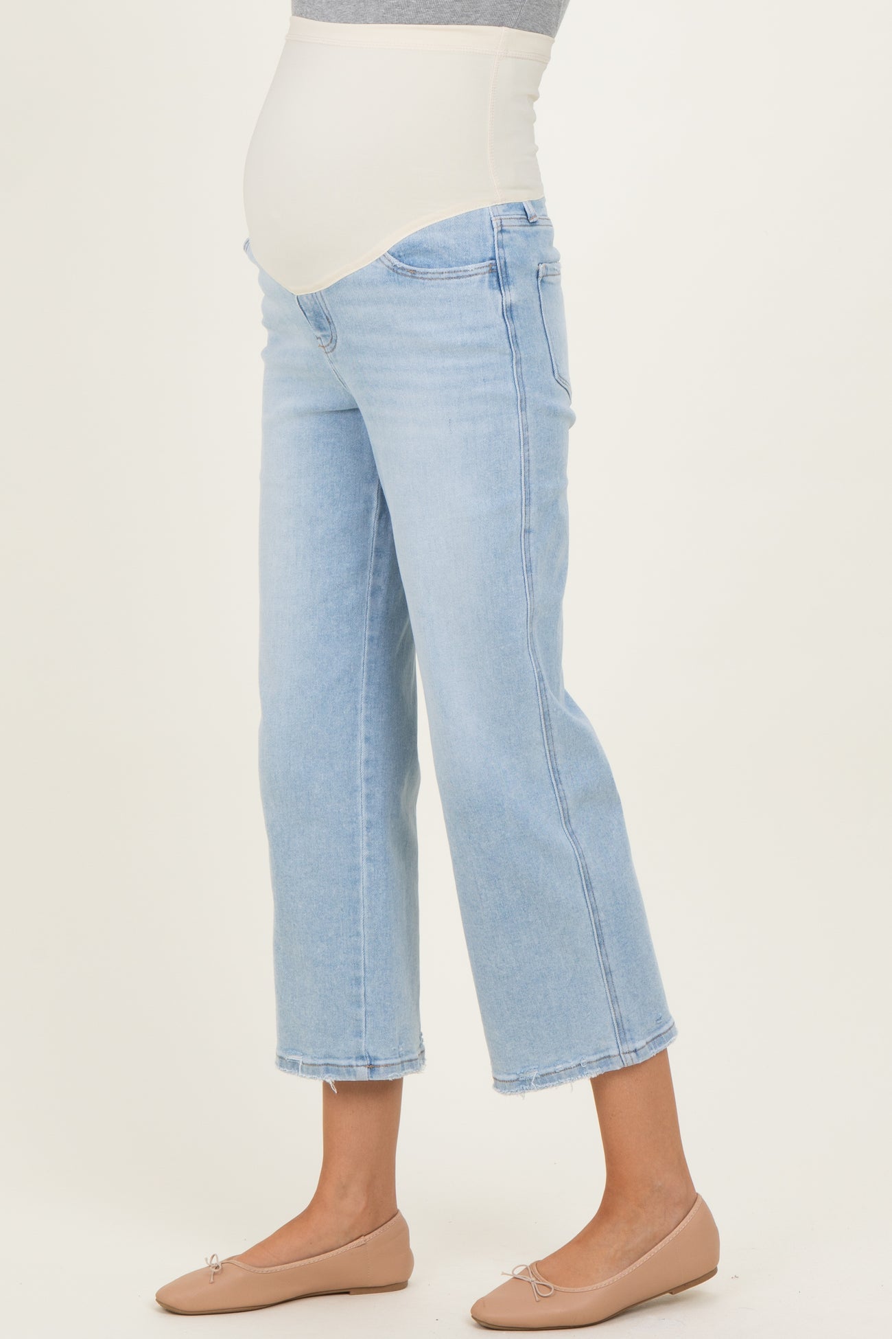 woman wearing light blue maternity jeans with a belly band and a visible baby bump, paired with nude ballet flats