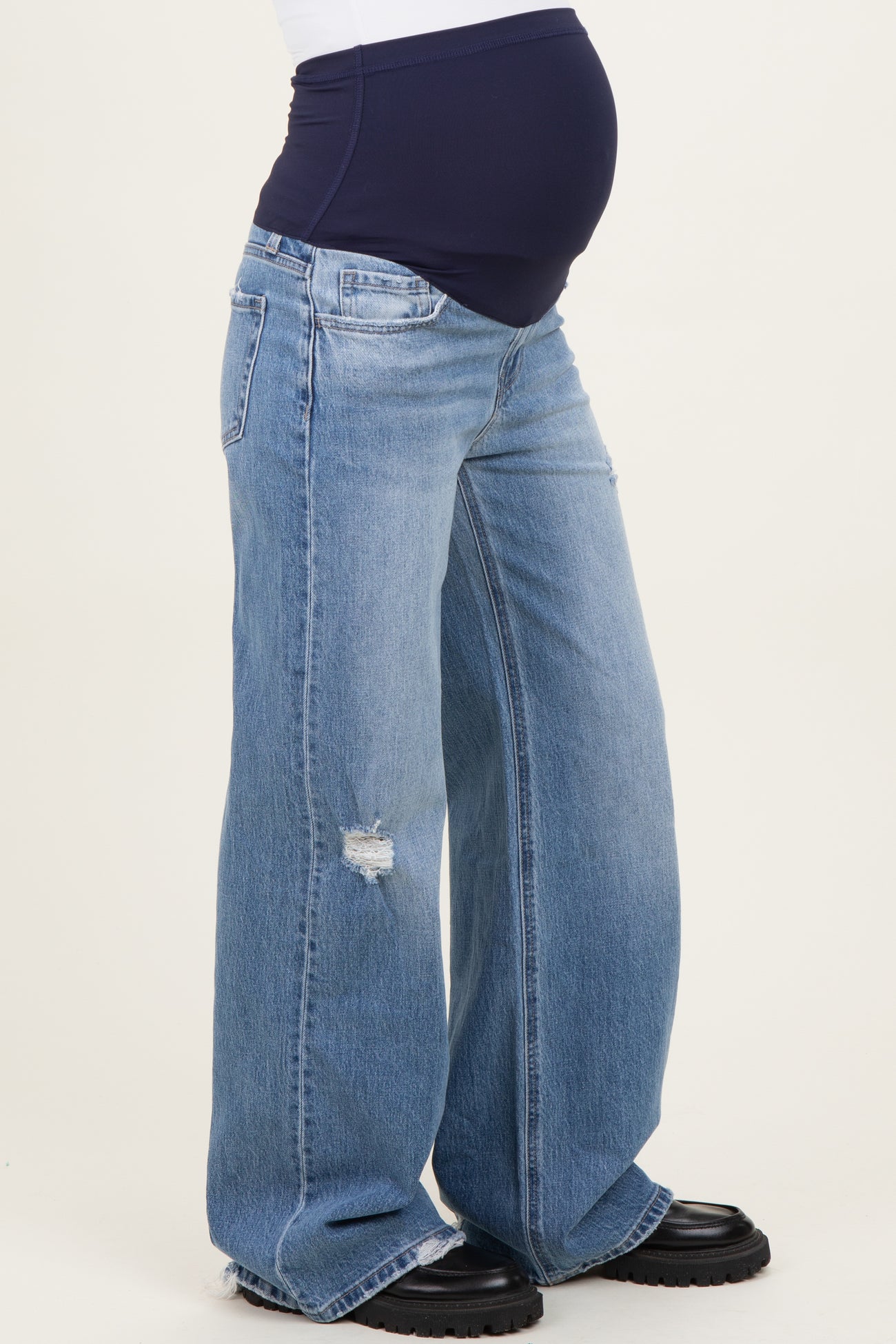 woman wearing light blue distressed maternity jeans with a dark navy waistband and visible baby bump