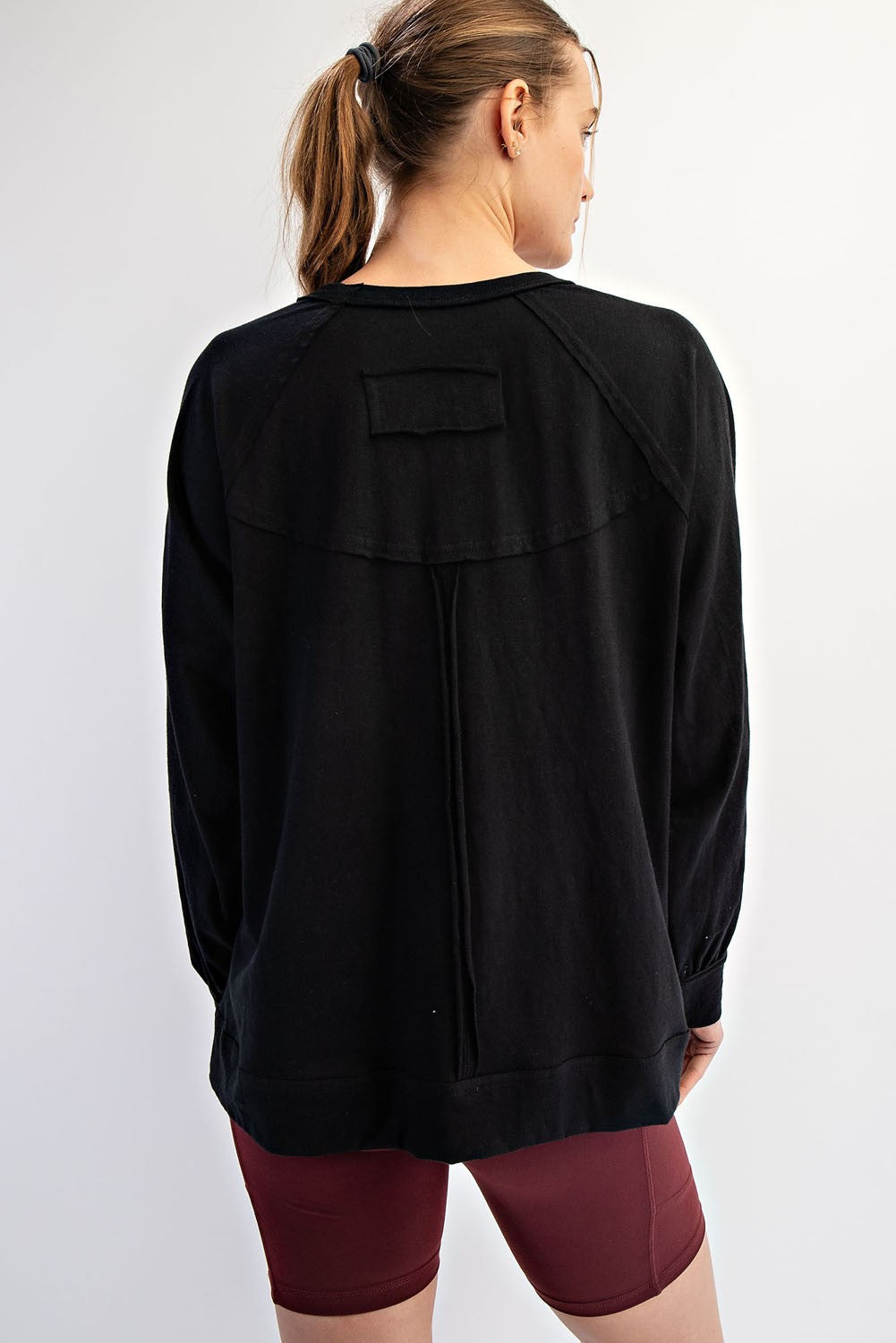 woman wearing a black oversized sweatshirt with a yoke detail and long sleeves, showing the back view