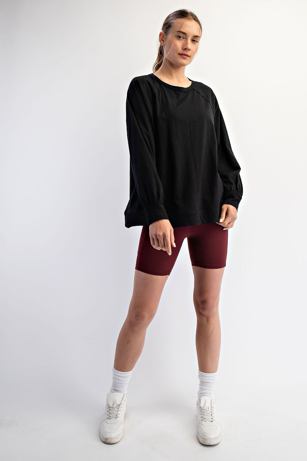 woman wearing a black oversized sweatshirt and burgundy bike shorts, standing with hands in pockets