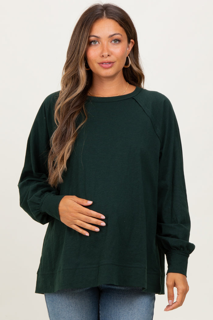 woman wearing a dark green long sleeve maternity top and holding her baby bump
