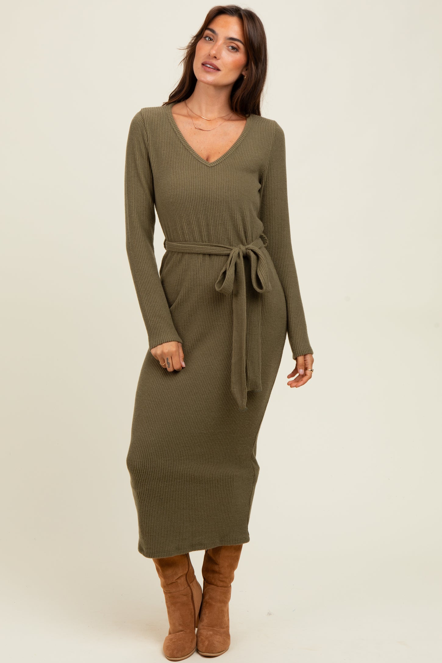 woman wearing an olive green ribbed midi dress with a v-neck and tie waist, standing and looking off to the side