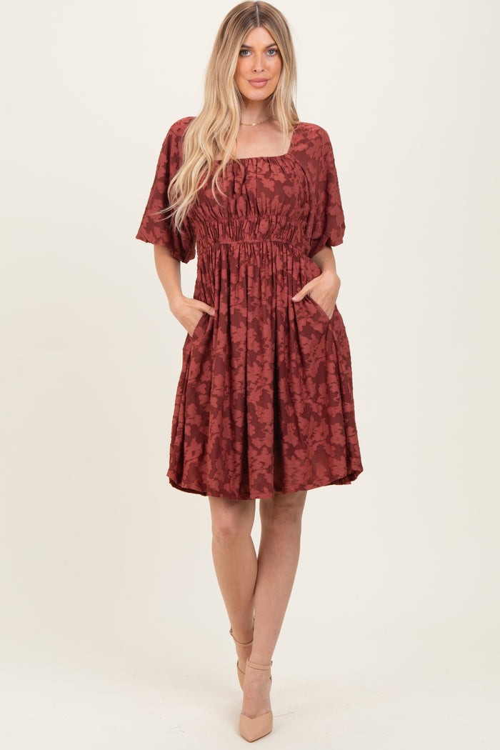 woman wearing a rust-colored floral short sleeve dress with a square neckline and pockets
