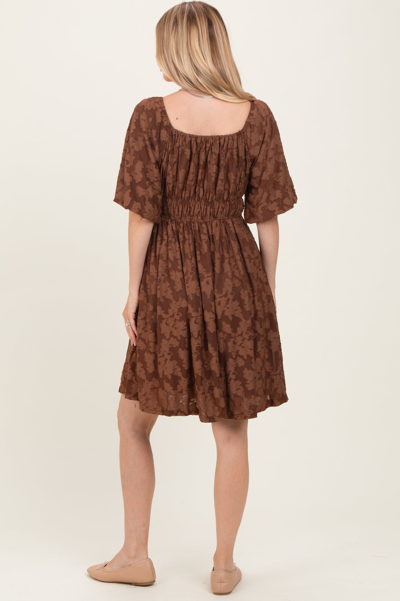 woman wearing a brown floral print short sleeve dress with a smocked waistband and a flared skirt, viewed from the back