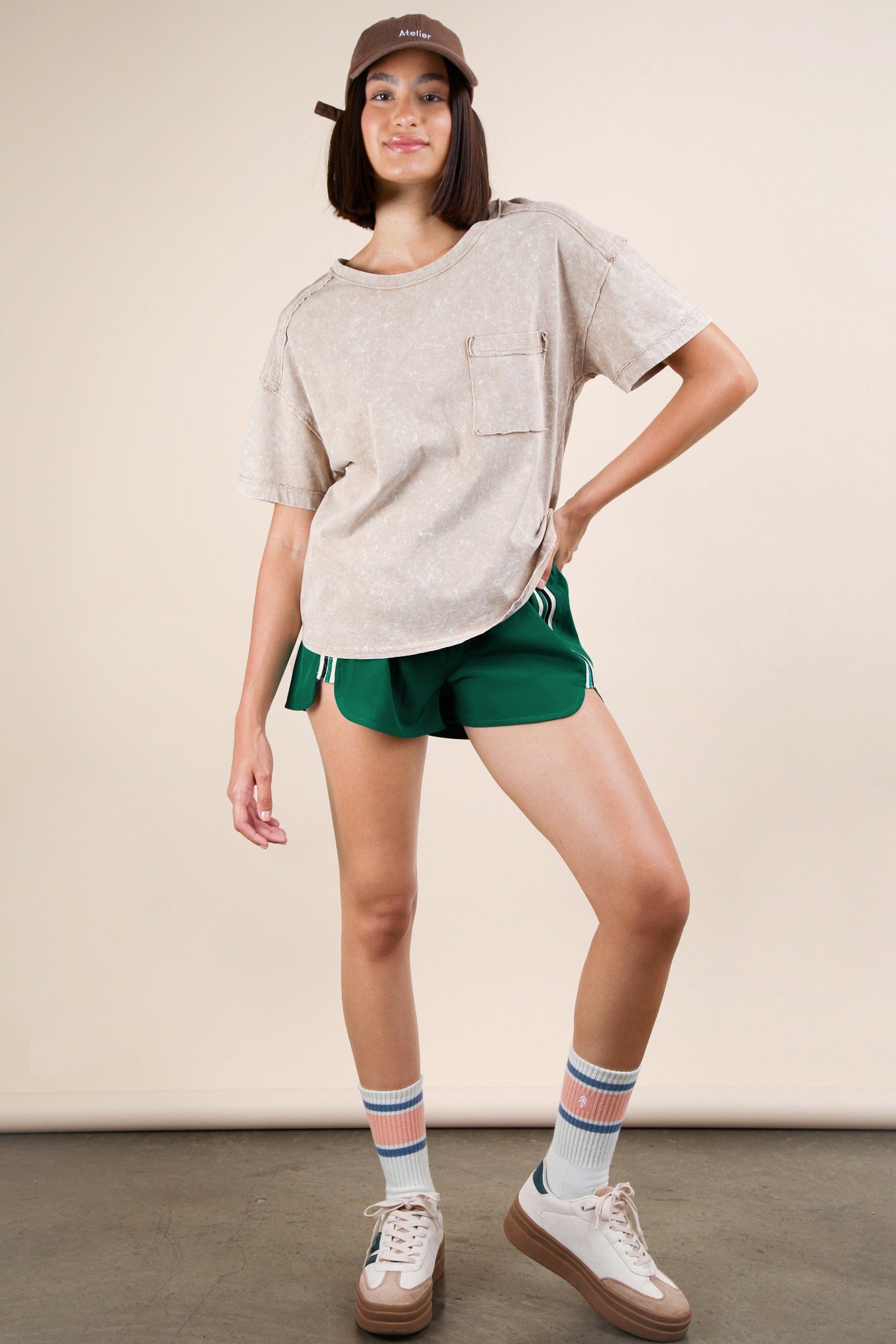 woman wearing a beige oversized t-shirt with a pocket, green athletic shorts, and sneakers with striped socks