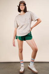woman wearing a beige oversized t-shirt with a pocket, green athletic shorts, and sneakers with striped socks