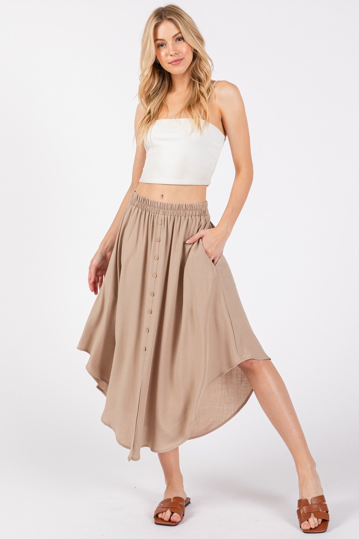 woman wearing a beige button-up maxi skirt with an elastic waistband and pockets, paired with a white cropped top