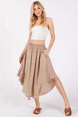 woman wearing a beige button-up maxi skirt with an elastic waistband and pockets, paired with a white cropped top