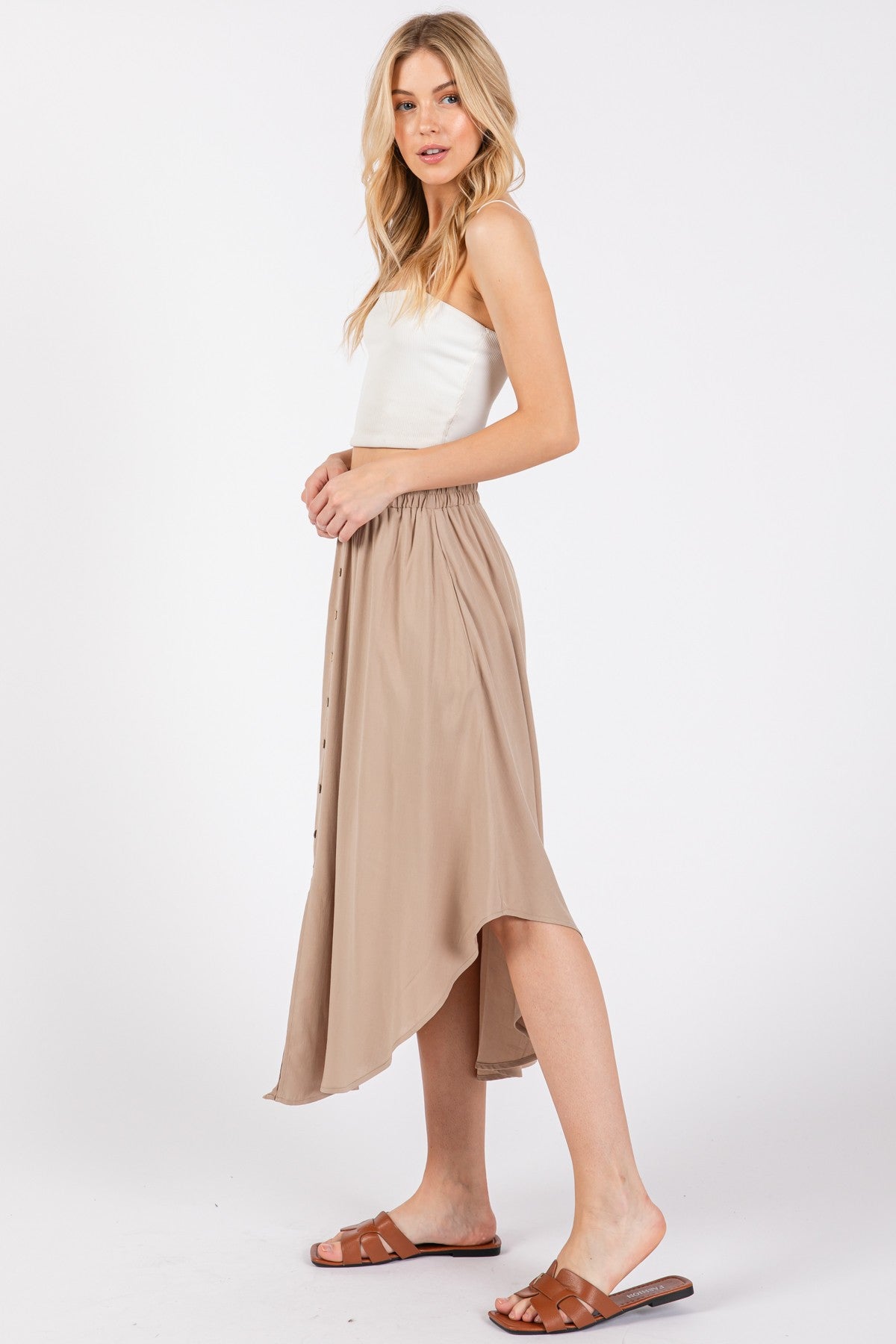 woman wearing a cream strapless top and a beige midi skirt with a high-low hem and button details